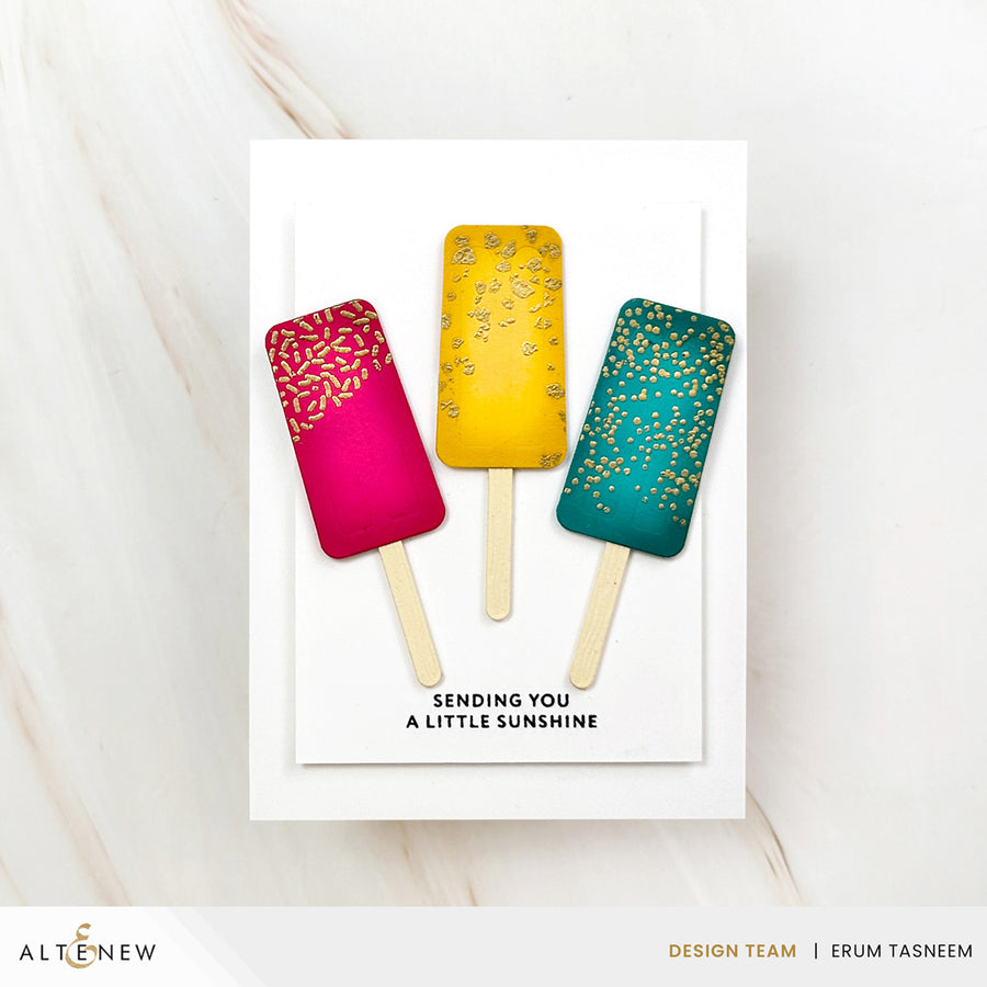 A handmade greeting card featuring three popsicle illustrations in pink, yellow, and teal with gold speckles, above the text 'SENDING YOU A LITTLE SUNSHINE'. The card is photographed on a light marble surface. Altenew Mini Delight: Sweet Popsicles Stamp & Die Set card ideas