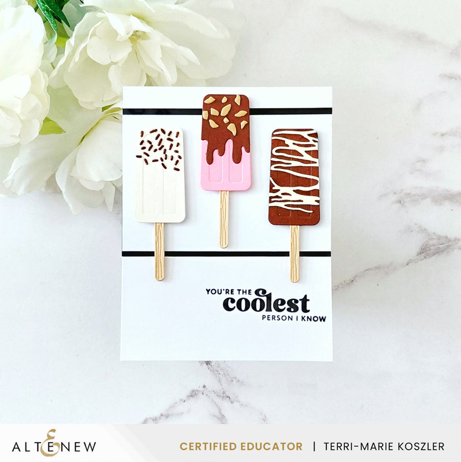 A handmade paper popsicle card featuring three decorated popsicles on wooden sticks, displayed on a white marble surface with white flowers in the background. The card reads 'YOU'RE THE COOLEST PERSON I KNOW'. Altenew Mini Delight: Sweet Popsicles Stamp & Die Set card ideas