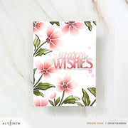 A handmade greeting card with a white background, featuring pink watercolor-style flowers with green leaves and the words 'warm WISHES' in pink script and block lettering. The card is photographed flat on a light marble surface, with brand text 'ALT&ENew' and 'DESIGN TEAM | ERUM TASNEEM' visible at the bottom. Altenew Painted Petals Stencil Set (3 in 1) card ideas