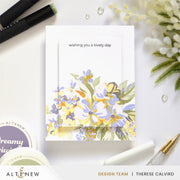 A handmade greeting card with the text 'wishing you a lovely day' and a watercolor-style floral design in yellow, lavender, and green, styled on a white surface with pens, decorative flowers, and Altenew branding visible. Altenew Build-A-Garden: Softly Sketched Blooms