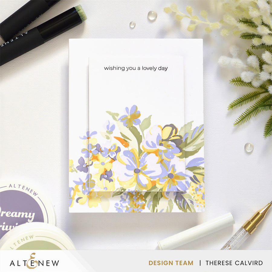 A handmade greeting card with the text 'wishing you a lovely day' and a watercolor-style floral design in yellow, lavender, and green, styled on a white surface with pens, decorative flowers, and Altenew branding visible. Altenew Build-A-Garden: Softly Sketched Blooms