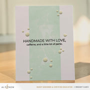 A handmade greeting card with a vertical mint green stripe on a white background, featuring embossed bubble details and the text 'HANDMADE WITH LOVE, caffeine, and a little bit of panic.' It is displayed standing on a wooden surface.