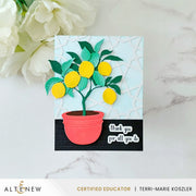 A handmade greeting card featuring a 3D layered lemon tree in a coral-pink pot, set against a light blue and black background with a white marble surface and white flowers in the corner. The card is branded with 'Altenew' at the bottom. Altenew Creative Cuts: Lemon Tree Layering Die Set card ideas