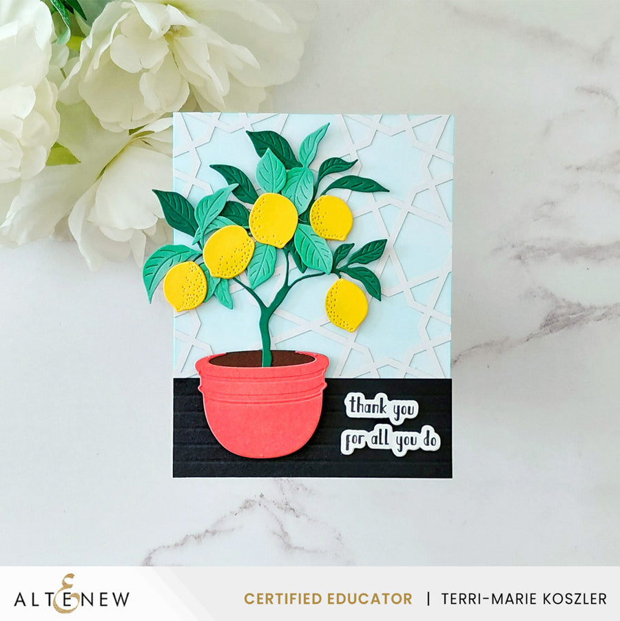 A handmade greeting card featuring a 3D layered lemon tree in a coral-pink pot, set against a light blue and black background with a white marble surface and white flowers in the corner. The card is branded with 'Altenew' at the bottom. Altenew Creative Cuts: Lemon Tree Layering Die Set card ideas