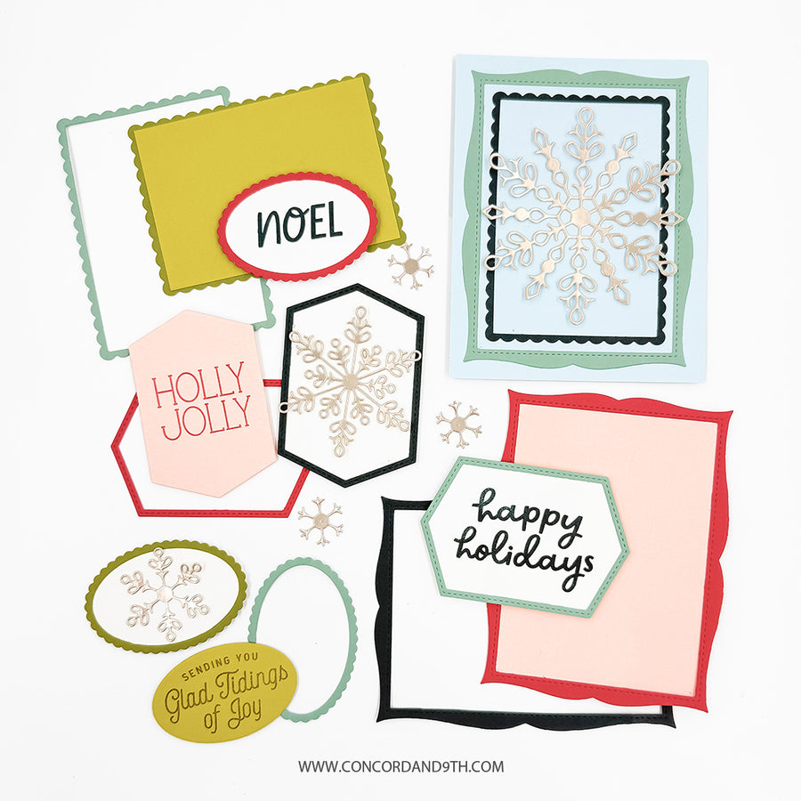 A flat lay of multiple handmade holiday greeting cards and decorative paper elements on a white background, including scalloped frames, snowflake cutouts, and phrases like “NOEL,” “HOLLY JOLLY,” and “Happy Holidays.”.