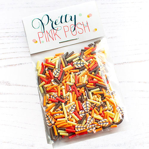 A clear plastic bag filled with colorful clay confetti and topped with a white paper label that reads 'Pretty Pink Posh' in teal and pink lettering, photographed on a white wood surface. Pretty Pink Posh Autumn Woods Clay Confetti