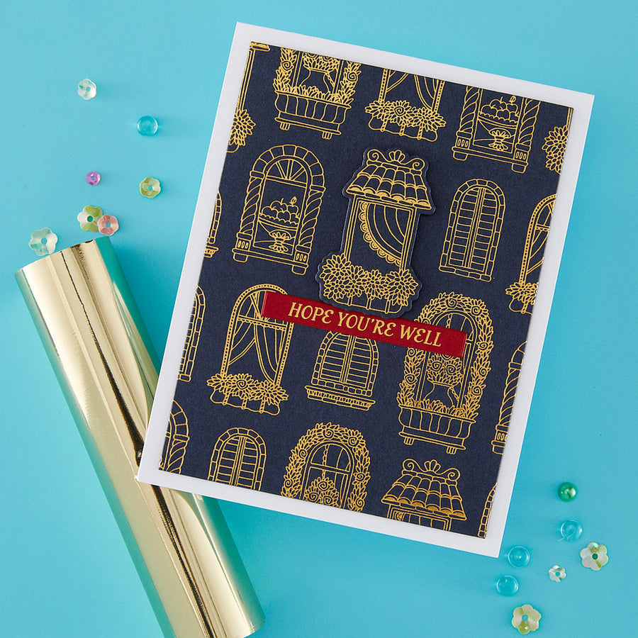 A handmade greeting card with a navy blue background, gold window patterns, and a red banner reading 'HOPE YOU'RE WELL', styled on a bright blue surface with a gold foil tube and scattered decorative beads.