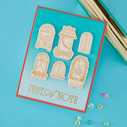 A turquoise card with six gold-toned window-shaped cutouts and the words 'JUST A NOTE' in gold, photographed on a bright blue background with small decorative beads and a metallic object at the top right.