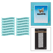 Crafting layout components including light blue banner stickers with birthday and congratulations messages, a turquoise greeting card with a butterfly design reading 'HELLO! BIG HUGS', and a black Spellbinders scrapbook sticker sheet. Spellbinders Signature Sentiments Press + Foil Plate & Die Set