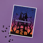 A rectangular Halloween handmade greeting card with a white border, featuring a haunted house, bare trees, bats, skulls, and the words “Happy Haunting” on a purple background with scattered black decorative dots. Using Spellbinders BetterPress Society August 2026 (Haunted Hollow Press Plate & Die Set + Add-on Stencil Bundle)