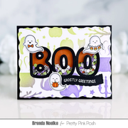 A handmade Halloween greeting card featuring the word 'BOO' in large orange and black letters filled with ghost-themed shaker confetti. The card has scalloped edges, a black border, and cute cartoon ghosts.