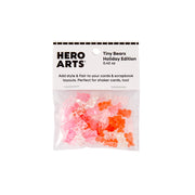 A clear plastic bag containing small translucent teddy bear-shaped embellishments in pink, coral, and orange, attached to a white Hero Arts Holiday Edition header card on a plain white background.