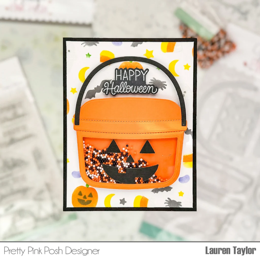 A handmade Halloween greeting card featuring an orange plastic bucket with black trim and a clear window filled with orange, black, and white glitter. The card has a white background decorated with yellow crescent moons, stars, and jack-o'-lanterns, and the words 'Happy Halloween' written at the top.
