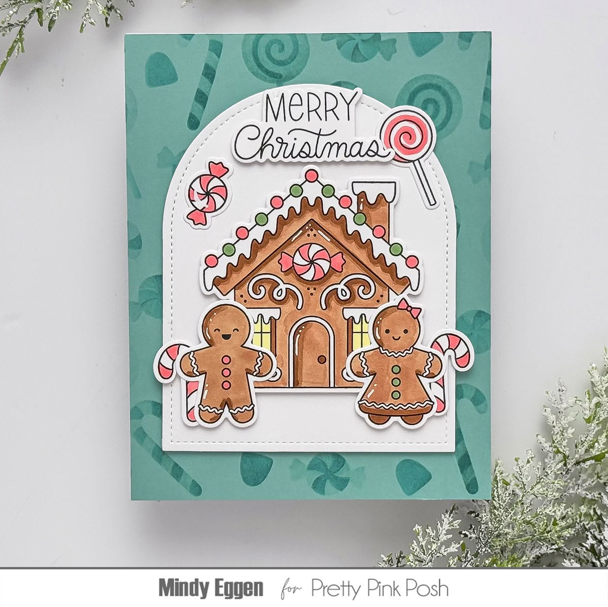 A handmade Christmas greeting card featuring a gingerbread house, two gingerbread people, candy canes, and a lollipop with the words 'Merry Christmas' at the top. The card is displayed against a white background with decorative foliage in the corners.