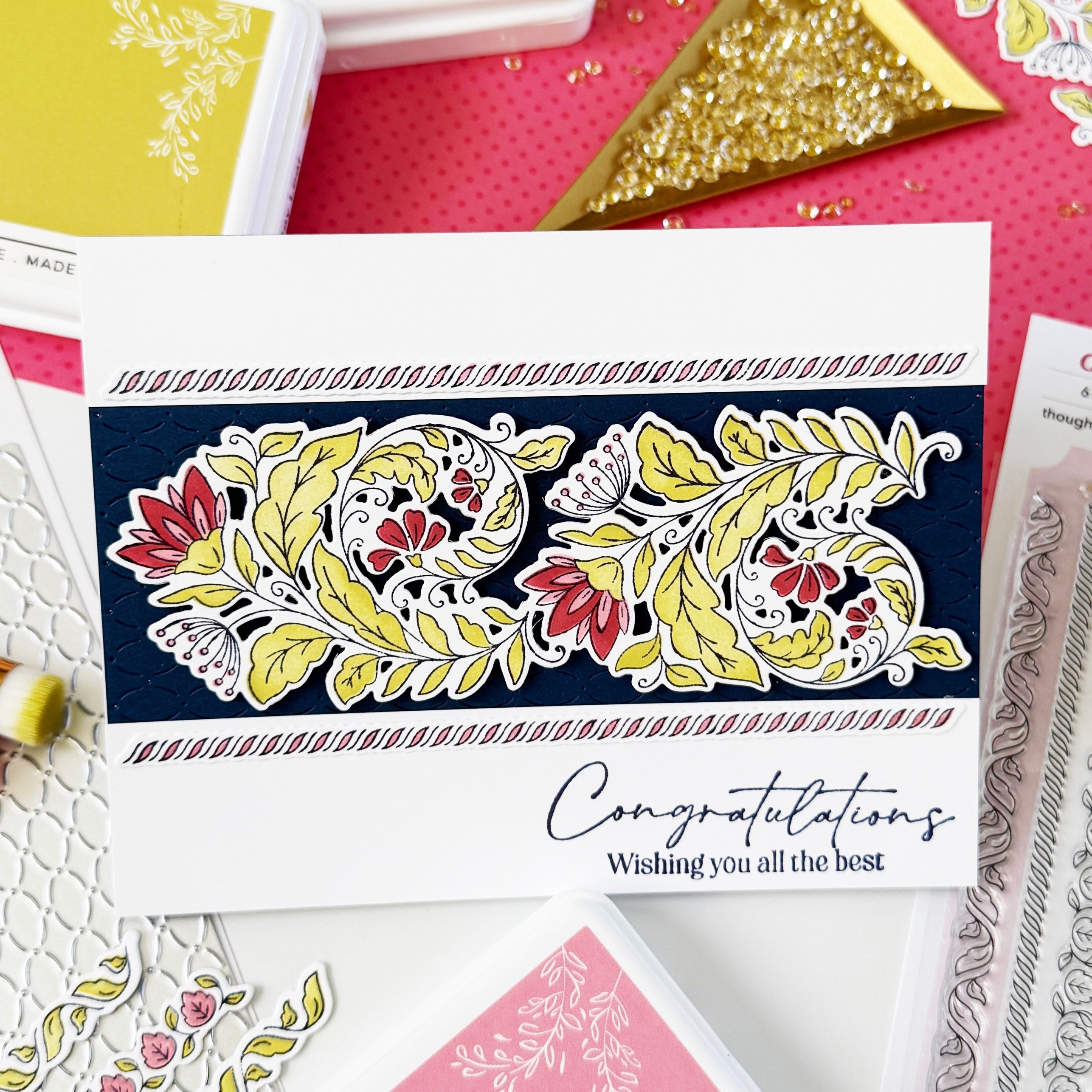 Handmade greeting card stamped in black in and die cut out. Die cut coloured in greens, reds and pinks and layered on a black rectangle panel and layered on top of a white rectangle card base with the sentiment 'Congratulations Wishing you all the best'