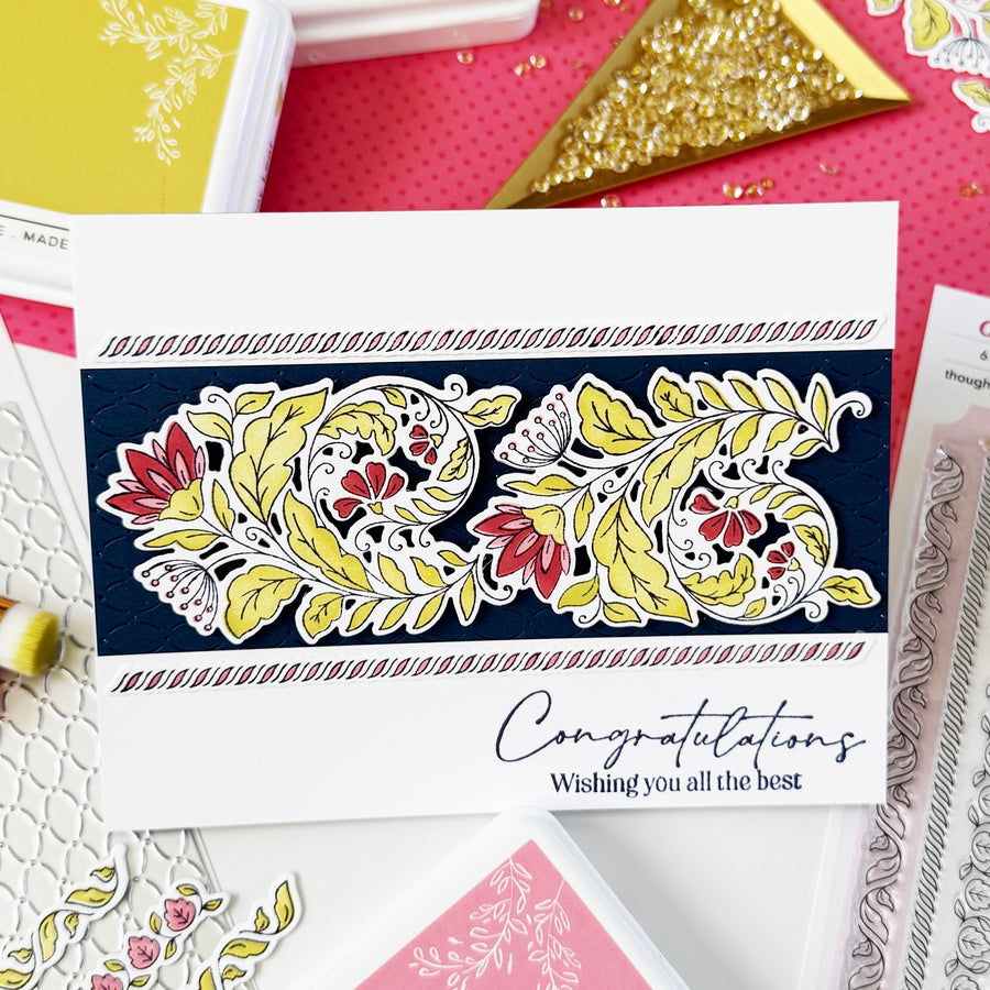 Handmade greeting card stamped in black in and die cut out. Die cut coloured in greens, reds and pinks and layered on a black rectangle panel and layered on top of a white rectangle card base with the sentiment 'Congratulations Wishing you all the best'
