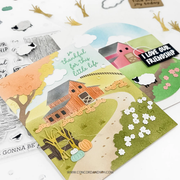 A handmade layered paper card featuring a farm scene with a red barn, trees, flowers, and sheep cutouts, displayed alongside clear stamp sheets on a white background.