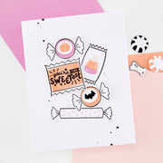 A white handmade greeting card featuring cute Halloween candy illustrations, styled on a pink and white background with small matching candy-shaped accessories nearby.