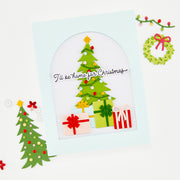 A handmade layered paper Christmas card with a light blue border, featuring a green paper Christmas tree with colorful ornaments, wrapped gift boxes, and the text 'I'll be home for Christmas'. The card is styled on a white background with decorative paper holiday elements. Using Hero Arts Beep Beep Holiday Extras Die Set