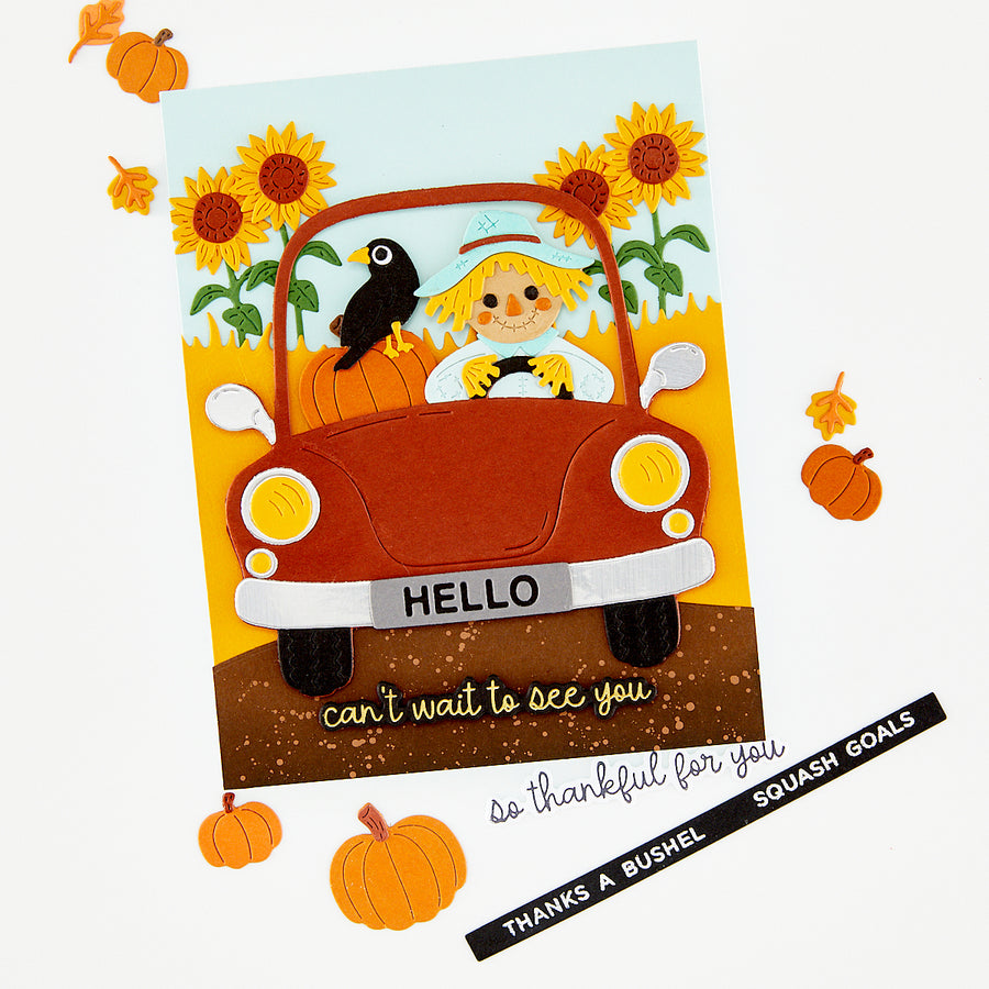 A handmade autumn-themed greeting card featuring a red car with a smiling child driving, a black bird on the roof, sunflowers, pumpkins, and the text 'HELLO' and 'can't wait to see you'. The card is shown on a white background with scattered orange pumpkins and a black ribbon that reads 'THANKS A BUSHEL' and 'SQUASH GOALS'. Hero Arts Beep Beep Leaf Peeper Die Set