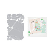 A die-cut craft set shown on a white background, with the gray metal cutting templates on the left and a sample card layout made from the dies on the right. The sample card features a decorated Christmas tree, a gnome, and small holiday accents.