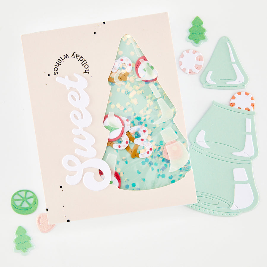 A flat-lay of a handmade greeting card with a die-cut white 'Sweet' script and a window showing a mint green Christmas tree filled with colorful confetti and candy decorations. Surrounding the card are matching mint green die-cut embellishments, including a Christmas tree, a candy cane, and a gingerbread man, on a clean white background.