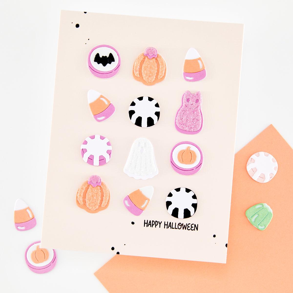 A Halloween-themed sticker sheet on a beige card, surrounded by scattered matching stickers. The sheet features candy corn, pumpkins, gummy bears, ghosts, black-and-white candy canes, and the text 'HAPPY HALLOWEEN' at the bottom.