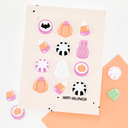 A Halloween-themed sticker sheet on a beige card, surrounded by scattered matching stickers. The sheet features candy corn, pumpkins, gummy bears, ghosts, black-and-white candy canes, and the text 'HAPPY HALLOWEEN' at the bottom.
