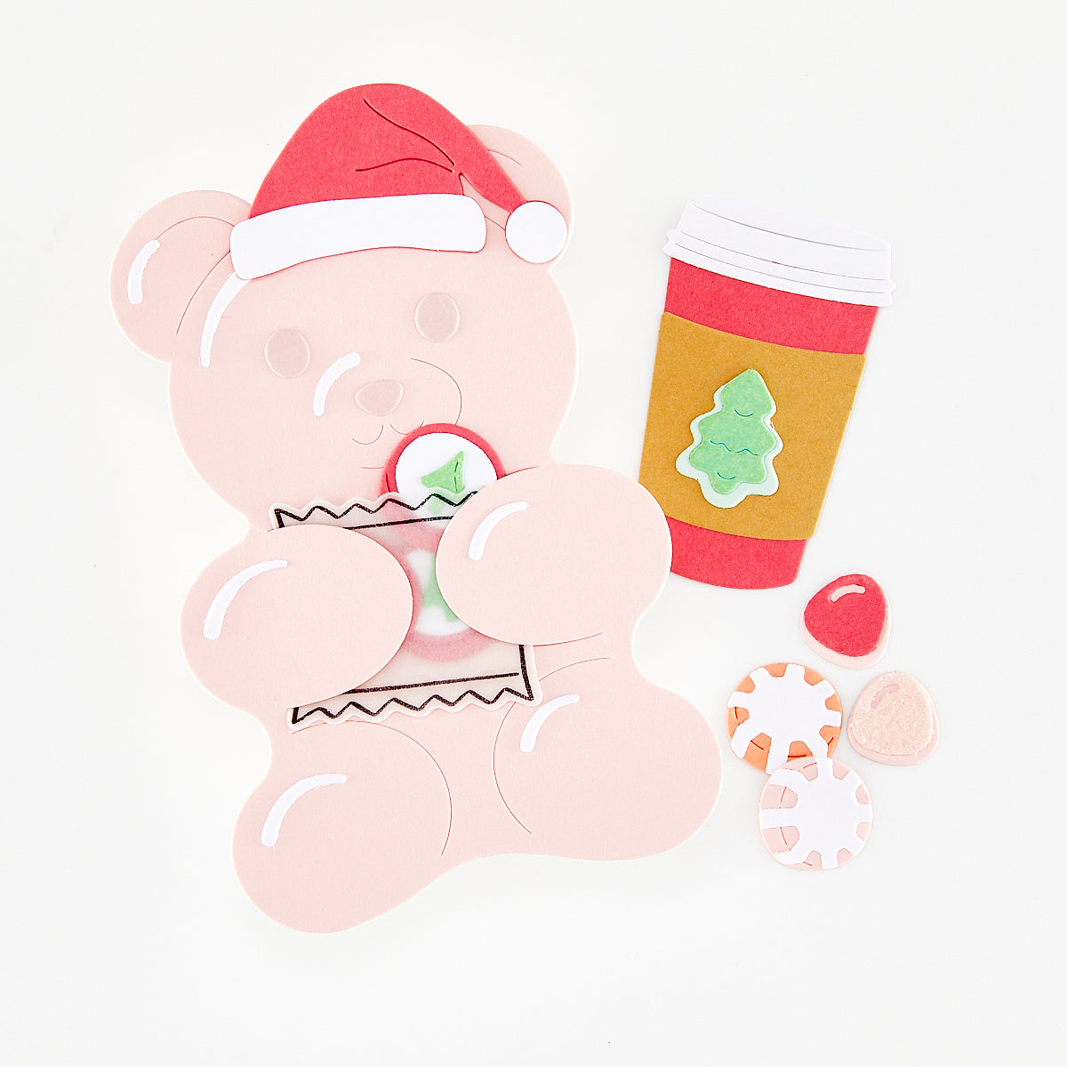 A Christmas-themed handmade elements featuring a light pink teddy bear wearing a red Santa hat, holding a wrapped candy, with a red and gold coffee cup and several small candy pieces on a clean white background.