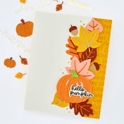 A handmade autumn-themed greeting card with layered paper pumpkins, leaves, acorns, and the words 'hello pumpkin' and 'thankful for you' on a white background.