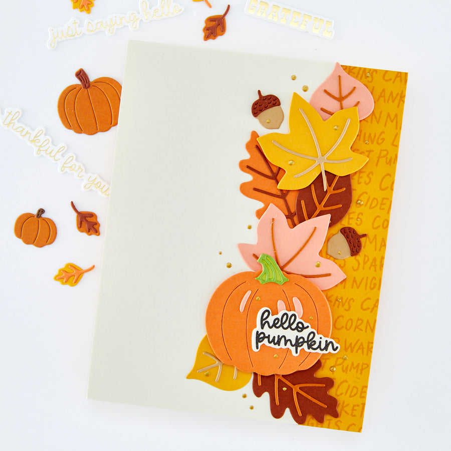 A handmade autumn-themed greeting card with layered paper pumpkins, leaves, acorns, and the words 'hello pumpkin' and 'thankful for you' on a white background.
