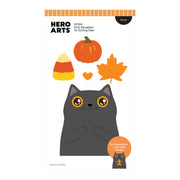 A product card for Hero Arts 'Kitty Squeezer' 15 cutting dies, featuring a cute cartoon gray cat with orange eyes and a pumpkin, candy corn, and maple leaf above it. The card includes product details, a die set label, and a small preview of the interactive cat holding a gingerbread man.