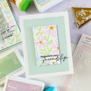 Handmade card with floral design and text on a crafting surface with stamps and tools.