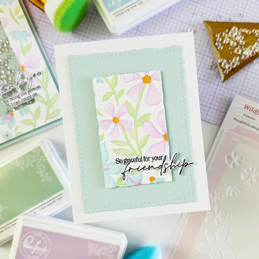 Handmade card with floral design and text on a crafting surface with stamps and tools.