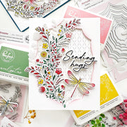 A handmade layered card with a floral cutout design and a dragonfly, surrounded by craft stamp and die packaging on a white background.