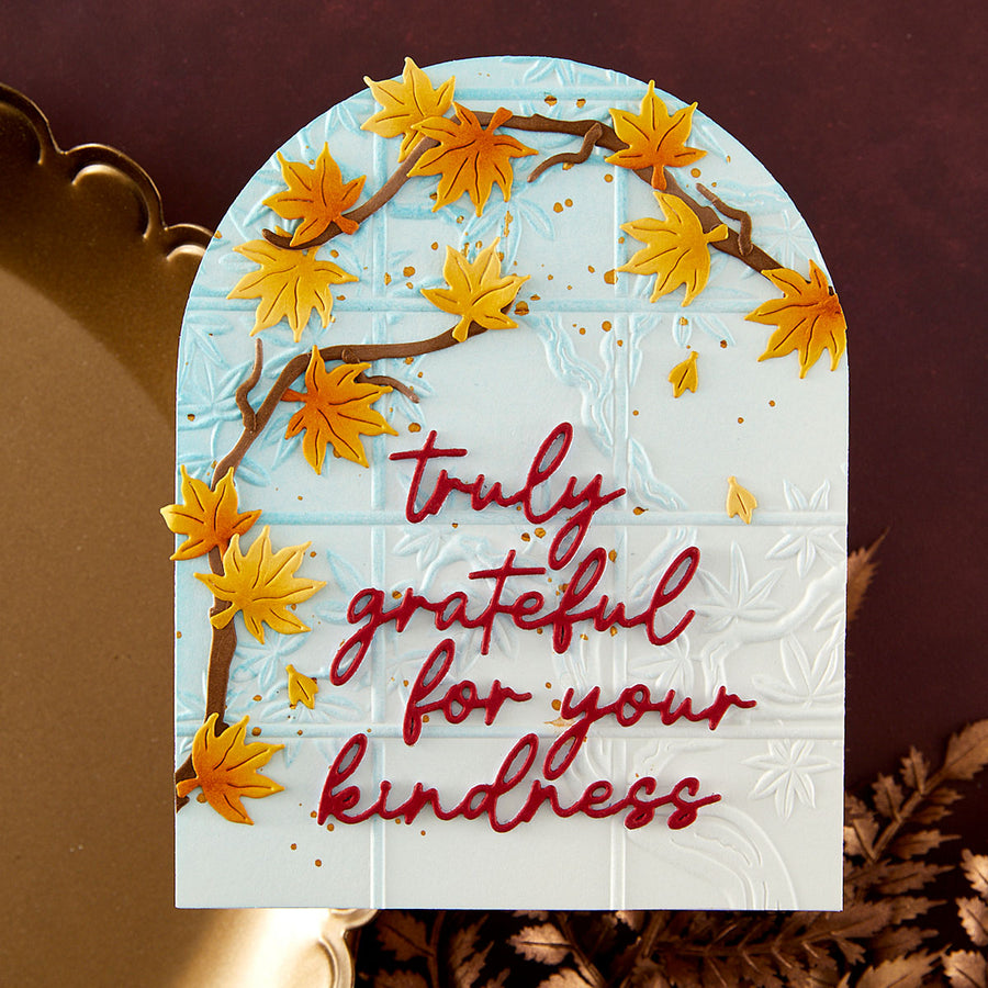 A handmade autumn-themed card featuring an arched white background with embossed floral details, decorated with 3D yellow maple leaves on brown branches and the phrase 'truly grateful for your kindness' in red script.