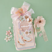 A decorative handmade card or art piece featuring a pair of pastel ice skates, embellished with 3D flowers, lace, and a large bow, displayed on a mint green background alongside matching floral embellishments. Also features Spellbinders Sparkling Trees 3D Embossing Folder by Frank Garcia