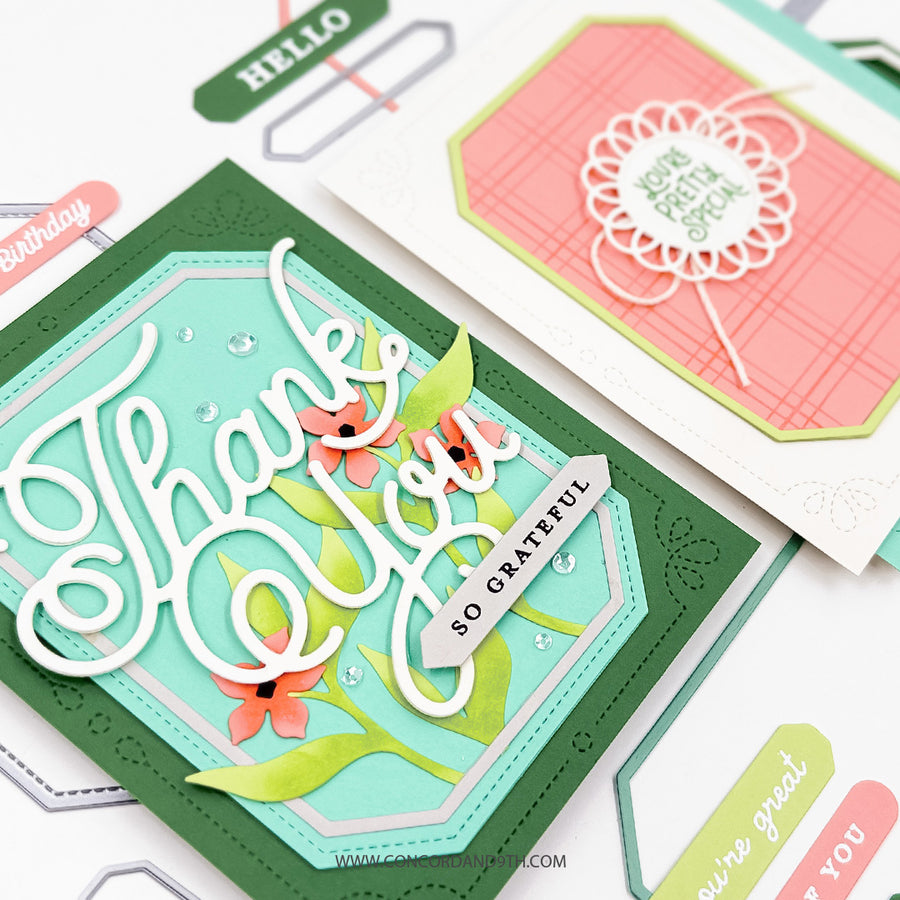 A close-up of a handmade layered greeting card with green and aqua borders, white script reading 'Thank You', floral die-cut elements, and a banner that says 'SO GRATEFUL'. Another partial card in coral and green is visible behind it on a white surface.