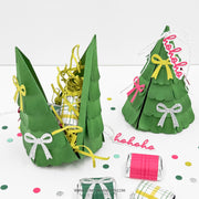 Green paper Christmas tree gift baskets filled with yellow shredded paper and wrapped treats, displayed on a white surface with colorful confetti and small wrapped gifts.
