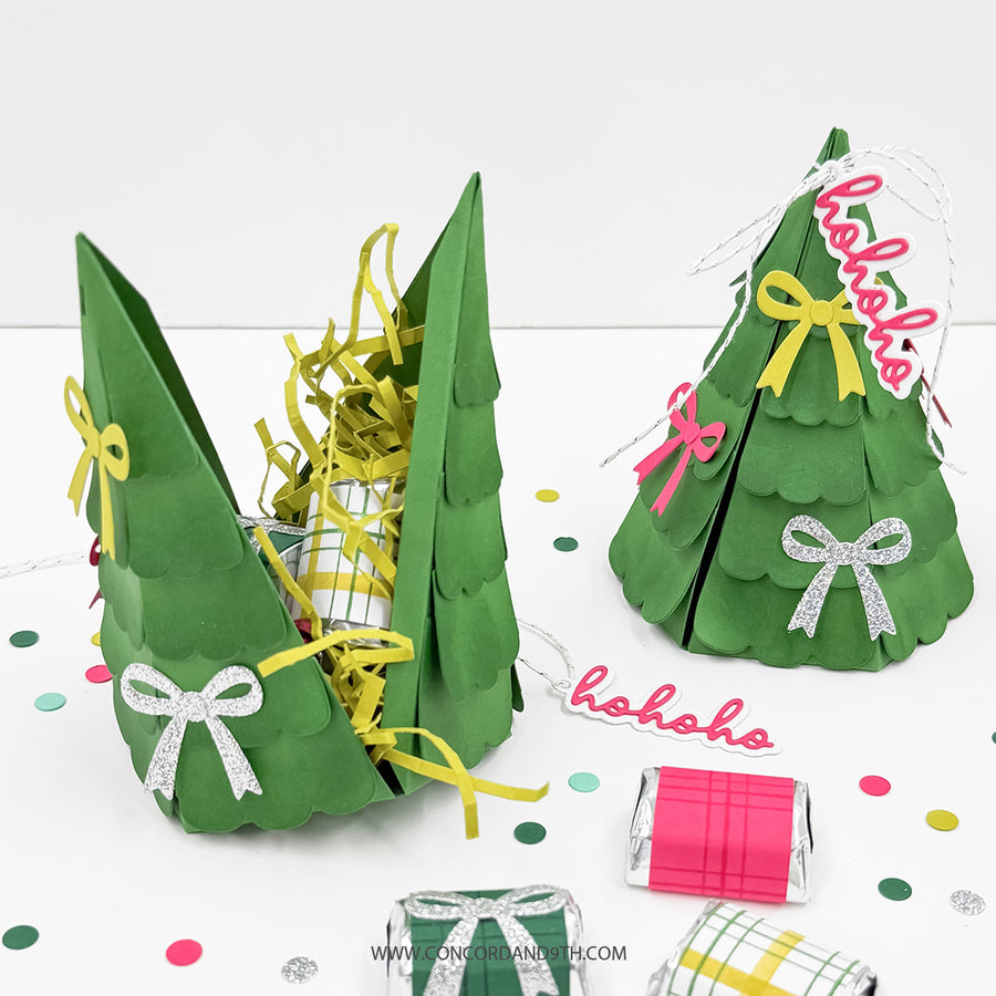 Green paper Christmas tree gift baskets filled with yellow shredded paper and wrapped treats, displayed on a white surface with colorful confetti and small wrapped gifts.