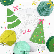 A flat lay of green paper Christmas tree craft templates and finished layered paper tree decorations in green, teal, and yellow, arranged around a white cardstock template with the word 'ho ho ho' on a white background.