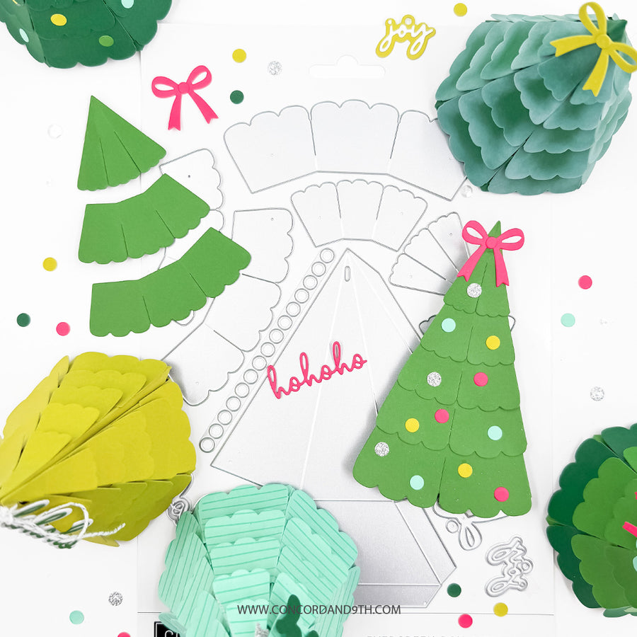A flat lay of green paper Christmas tree craft templates and finished layered paper tree decorations in green, teal, and yellow, arranged around a white cardstock template with the word 'ho ho ho' on a white background.