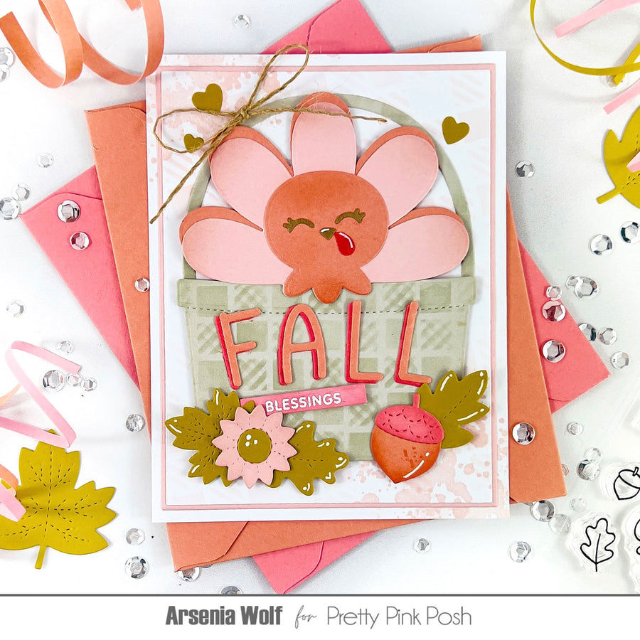A handmade autumn-themed greeting card featuring a smiling pink and orange turkey in a patterned basket, with the word 'FALL' in 3D letters and 'Blessings' on a pink banner. The card is styled with layered pink and orange envelopes, gold ribbon, and scattered rhinestones on a white background.
