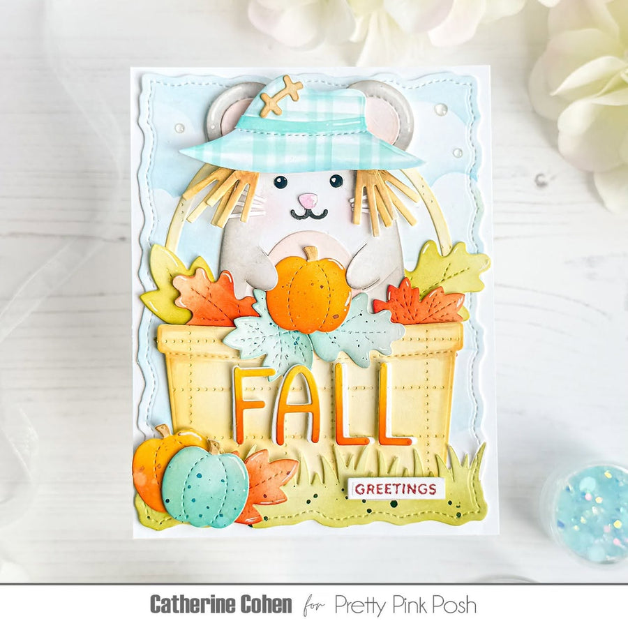 A handmade autumn greeting card featuring a white mouse in a plaid hat holding a pumpkin, surrounded by fall leaves, pumpkins, and the word 'FALL' in large letters. The card is displayed on a light wood surface with decorative flowers and a small blue orb in the background.