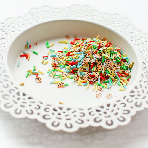 Multicolor miniature clay confetti with tiny printed illustrations, scattered on a white ceramic plate with a scalloped lace edge. Pretty Pink Posh Fall Fling Clay Confetti