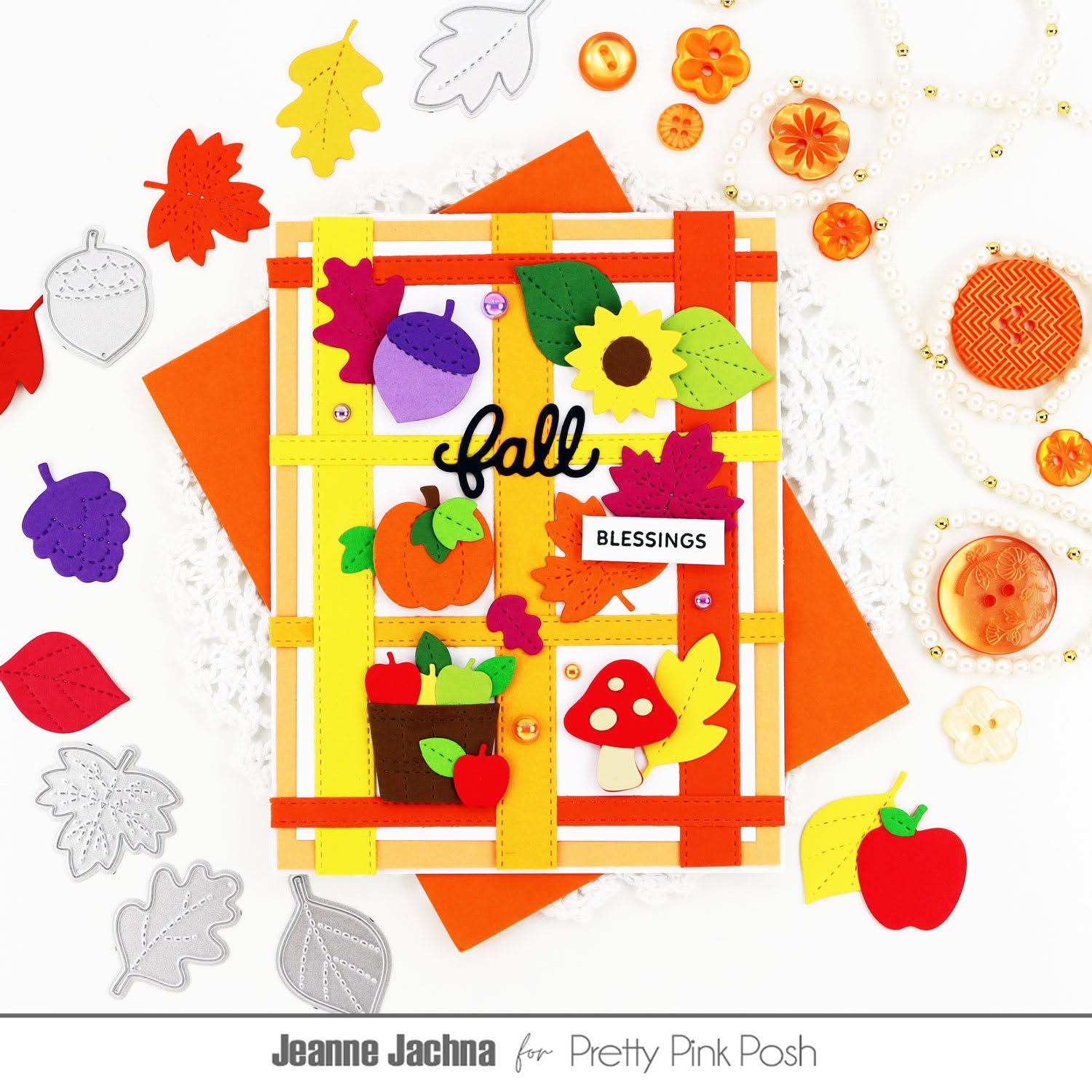 An autumn-themed handmade card featuring a plaid orange and yellow border with felt fall elements including acorns, leaves, a sunflower, mushrooms, and a pumpkin. The card is displayed on orange paper with scattered felt cutouts and decorative pearls around it.