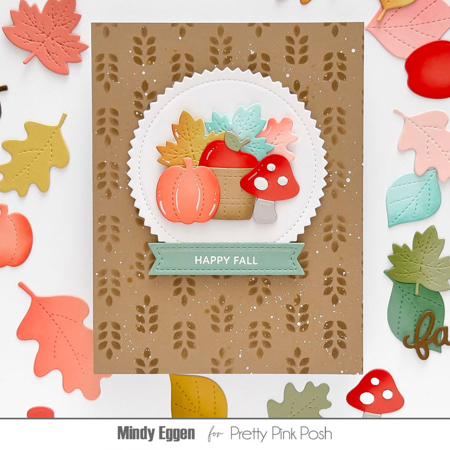 A handmade autumn-themed card featuring a brown kraft background with a leaf pattern, a white scalloped circle, layered fall leaves, pumpkins, mushrooms, and a mint banner reading 'HAPPY FALL.' The card is photographed on a white surface surrounded by scattered matching fall leaf and acorn embellishments.