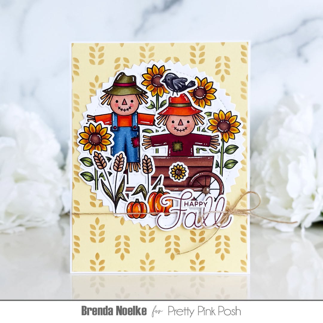 A handmade autumn-themed greeting card featuring two scarecrows, sunflowers, pumpkins, wheat, and a bird, with 'Happy Fall' written on a pale yellow patterned card. The card is wrapped in twine and displayed on a light marble surface with white flowers in the background.
