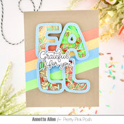 A handmade greeting card featuring layered die-cut letters spelling 'FALL' filled with a colorful autumn leaf pattern, layered over diagonal pastel stripes and a central script reading 'Grateful for you!'. The card is photographed on a white surface with decorative dried flowers and sprinkles.