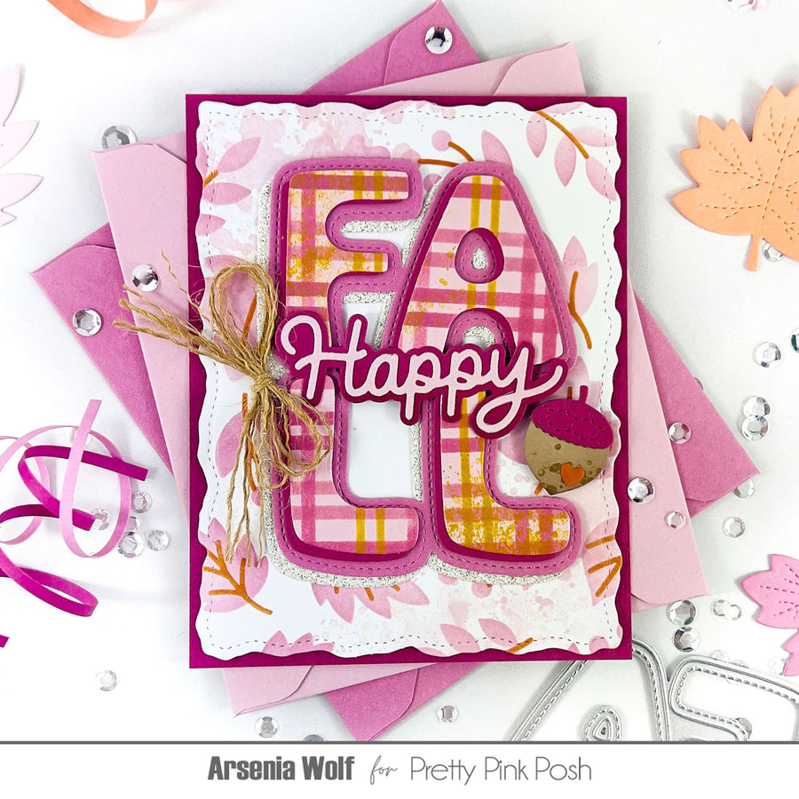 A handmade layered greeting card with the word 'Happy' in layered die-cut letters, decorated with pink and orange plaid patterns, a small acorn embellishment, and twine, displayed on top of pink cardstock sheets with scattered rhinestones and autumn leaf cutouts.
